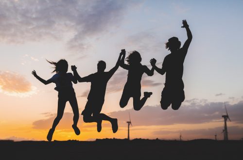 happy hipster friends company silhouettes on sunset desert landscape jumping together holding hands having fun on vacation, young people traveling